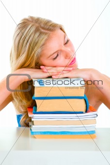 Tired girl sitting at desk and sleeping on piles of books
