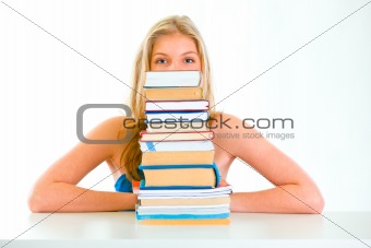 Sitting at table teen girl looking out of pile of book
