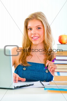Smiling pretty girl sitting at table with books and laptop
