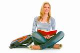 Smiling teen girl with backpack sitting on floor and reading schoolbook
