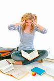 Teen girl sitting on floor among schoolbooks and studying hard
