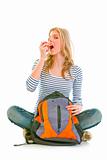 Pretty girl sitting on floor with schoolbag and eating apple
