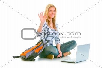 Girl sitting on floor with backpack and laptop showing ok gesture

