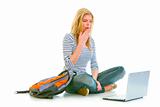 Amazed teen girl sitting on floor with backpack and looking on laptop
