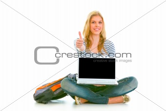 Smiling pretty girl sitting on floor with laptop and showing thumbs up
