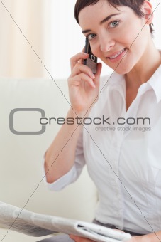 Close up of a brunette woman with a phone and a newspaper