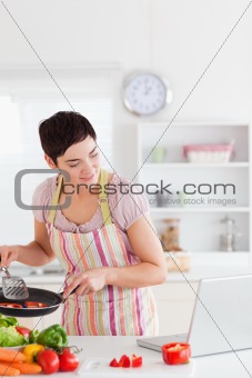 Smiling woman cooking with receipt on laptop