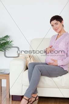 Pretty pregnant woman sitting on a sofa touching her belly