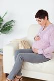 Brunette short-haired pregnant woman sitting on a sofa touching her belly