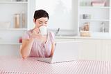 Woman drinking coffee while working with a laptop