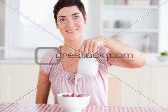 Woman pouring cream over strawberries looking into the camera