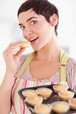 Charming brunette woman showing muffins while eating one