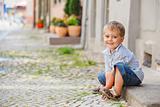 little boy sits on the doorstep on a city street