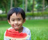 cute asian boy eating watermelon on the grass
