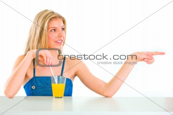 Cheerful teenager with orange juice pointing in corner
