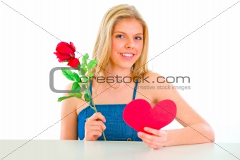 Lovely girl sitting at table with rose and Valentine heart
