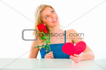 Dreaming girl sitting at table with rose and Valentine heart
