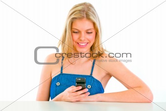 Cheerful teenager sitting at table and reading sms
