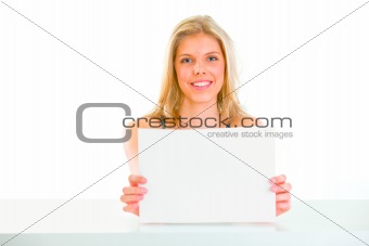 Lovely girl sitting at table and holding blank paper

