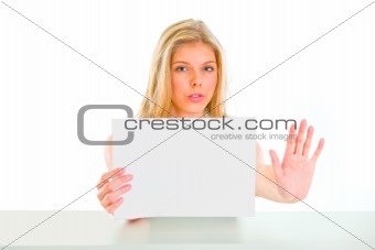 Concerned girl holding blank paper and showing stop gesture
