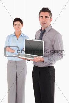 Portrait of a man showing a laptop while his colleague is posing