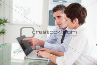 Man pointing at something to his secretary on a notebook