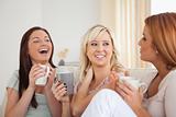 Laughing women sitting on a sofa with cups