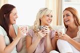 Cheering women sitting on a sofa with cups