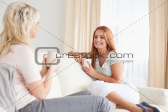 Cheerful young women sitting on a sofa holding cups