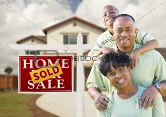 Happy African American Family in Front of New House and Sold Real Estate Sign.