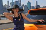 Young sexy girl posing in enening dress and hat by metallic orange sport car