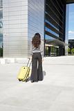 businesswoman with yellow suitcase in front of business building