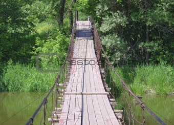 Old suspension walk bridge across river in the  forest