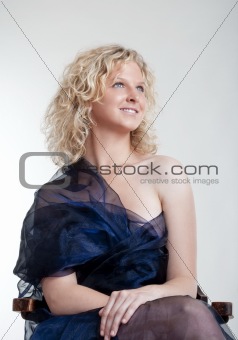 young woman in evening dress sitting in the chair smiling - isolated on light gray