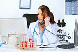 Concerned doctor woman talking on phone and looking in monitor
