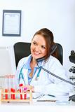 Smiling doctor woman talking on phone and looking in monitor
