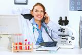 Relaxed doctor woman sitting at office table and talking on phone
