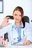 Authoritative doctor woman sitting at office table and holding blank business card
