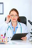 Doctor woman sitting at office table and looking in clipboard
