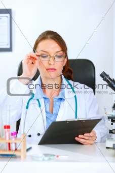 Doctor woman sitting at office table and looking in clipboard
