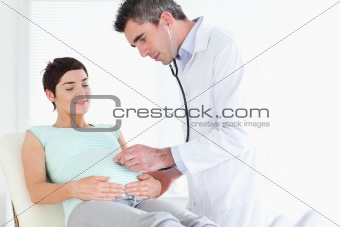 Doctor listening into the woman's tummy with a stethoscope