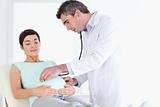 Doctor examining the cute woman's tummy with a stethoscope
