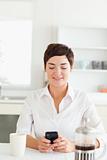 Woman with mobile phone and coffee in kitchen