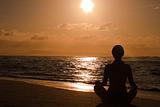 Female meditating on the beach at sunrise