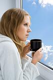 young beautiful girl drinking coffee by the window in the morning