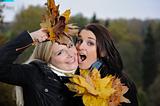 two beautiful girl friends with autumn leafs in a park