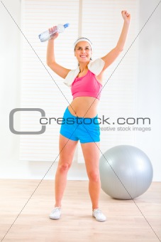 Smiling fitness girl with towel and bottle of water rejoicing success
