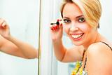 Smiling woman in bathroom applying mascara
