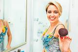 Cheerful pretty woman in bathroom extends fluffy brush in camera
