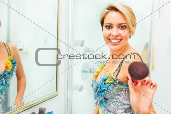 Cheerful pretty woman in bathroom extends fluffy brush in camera
